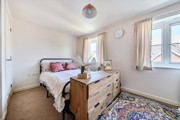 Bedroom with a bed, chest of drawers, rug and two windows.
