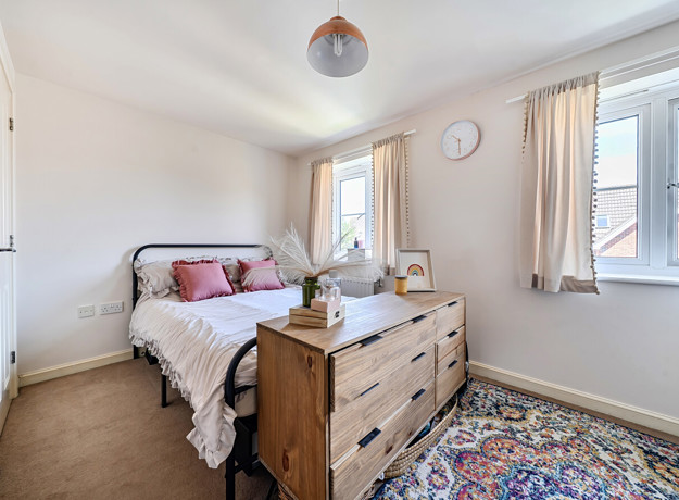 Bedroom with a bed, chest of drawers, rug and two windows.