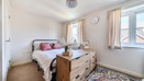 Bedroom with a bed, chest of drawers, rug and two windows.