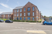 Apartment building with brick exterior, landscaped frontage, and parked cars.