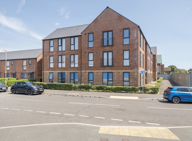 Apartment building with brick exterior, landscaped frontage, and parked cars.