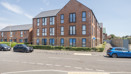 Apartment building with brick exterior, landscaped frontage, and parked cars.