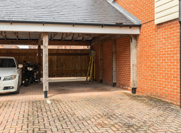 Carport with parked vehicle, brick walls, and paved driveway.