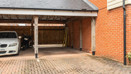 Carport with parked vehicle, brick walls, and paved driveway.