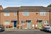 Row of brick terraced houses with front doors and parked cars.