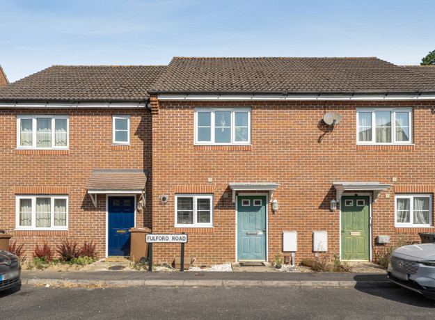 Row of brick terraced houses with front doors and parked cars.