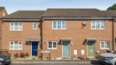 Row of brick terraced houses with front doors and parked cars.
