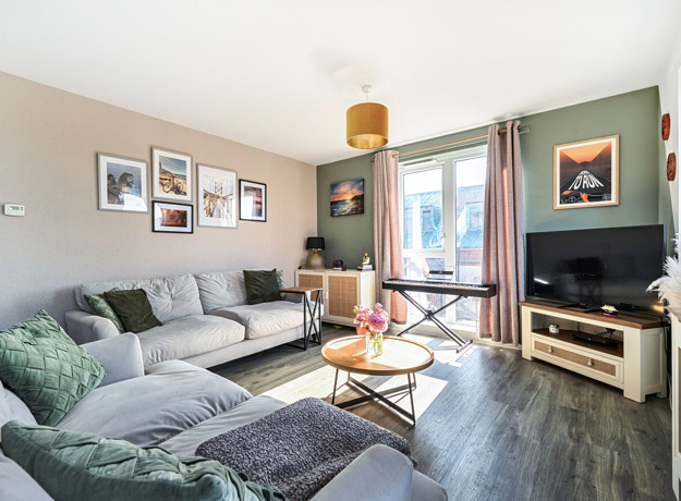 Living room with corner sofa, television, window and framed wall pictures.