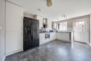 Kitchen with white cabinets, black appliances, dark vinyl flooring and door to back garden