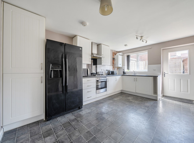 Kitchen with white cabinets, black appliances, dark vinyl flooring and door to back garden