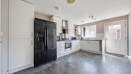 Kitchen with white cabinets, black appliances, dark vinyl flooring and door to back garden