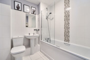Bathroom with white suite, tiled walls, bathtub, and overhead shower.