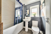 Modern bathroom with bathtub, sink and toilet, with a dark wall and beige tiles.