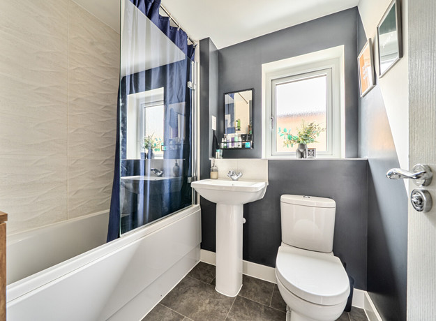 Modern bathroom with bathtub, sink and toilet, with a dark wall and beige tiles.