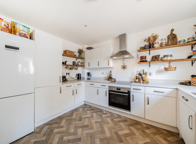 White kitchen with fitted units, open shelving and integrated oven.