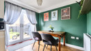 Dining area with table and chairs near french doors with curtains and green wall.