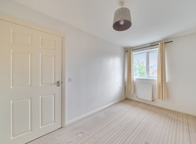 Empty bedroom with carpeted floor, light walls, and window with curtains.
