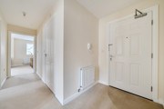 Hallway with doors, radiator, and light walls leading through home.