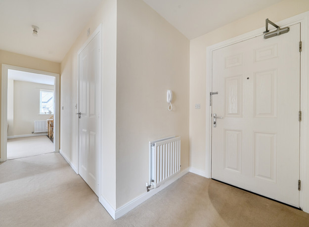 Hallway with doors, radiator, and light walls leading through home.