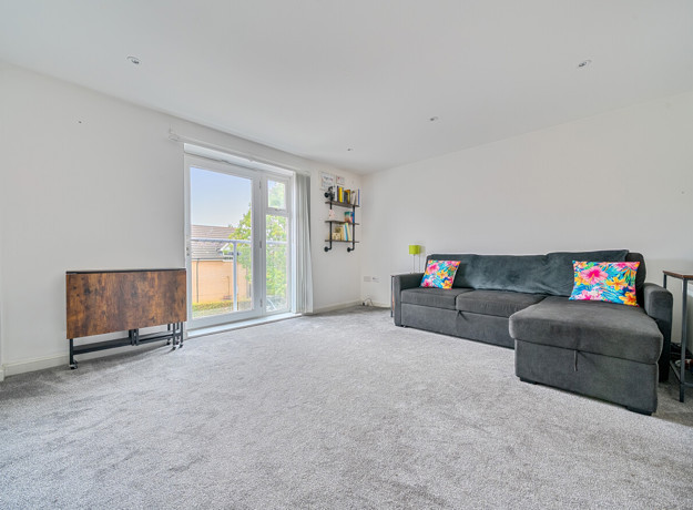 Spacious living room with grey carpet, large window, radiator, and corner sofa.