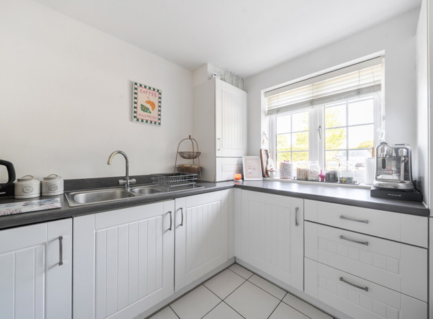 Kitchen with white cabinets, black worktops, sink and window.