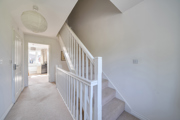 Hallway with staircase, handrail, carpet, and ceiling light fixture in neutral decor.