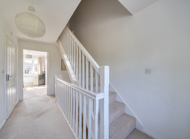 Hallway with staircase, handrail, carpet, and ceiling light fixture in neutral decor.