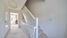 Hallway with staircase, handrail, carpet, and ceiling light fixture in neutral decor.