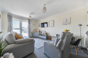 Living room with sofa, armchair, TV, cabinets, balcony doors and a dining table.
