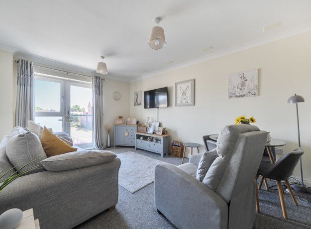 Living room with sofa, armchair, TV, cabinets, balcony doors and a dining table.