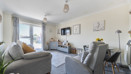 Living room with sofa, armchair, TV, cabinets, balcony doors and a dining table.