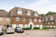 Row of brick terraced houses with parked cars in a shared driveway.