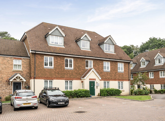 Row of brick terraced houses with parked cars in a shared driveway.