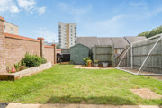 Back garden with lawn, fence panels, shed and surrounding buildings.