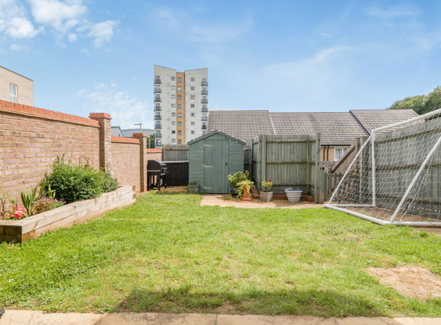Back garden with lawn, fence panels, shed and surrounding buildings.