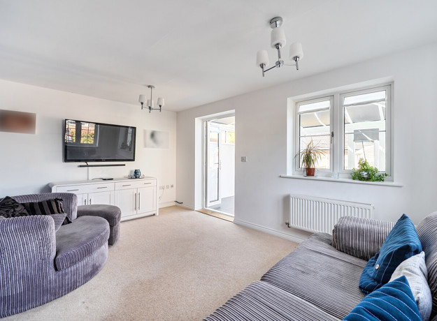 Bright living room with grey sofas, beige carpet, large window and French doors leading to conservatory.