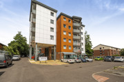 Tall apartment building with parking spaces and cars at the entrance.