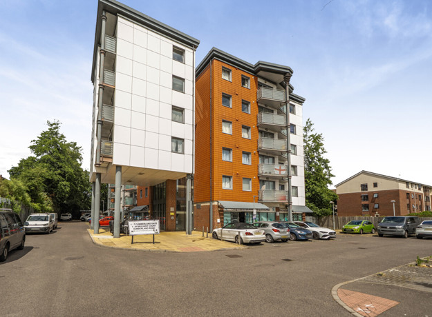 Tall apartment building with parking spaces and cars at the entrance.