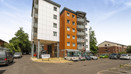 Tall apartment building with parking spaces and cars at the entrance.