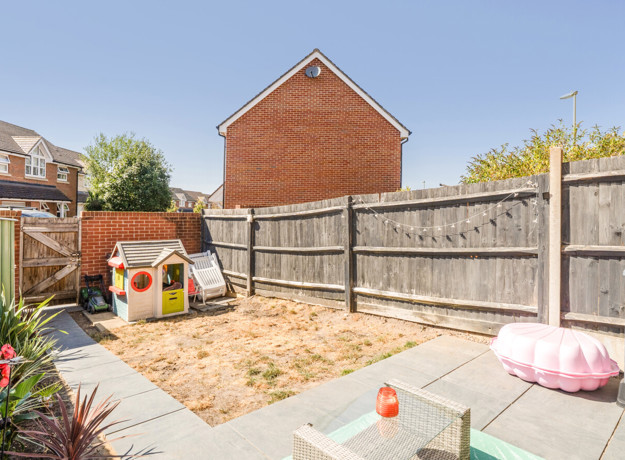 Enclosed garden with paved patio, fencing and playhouse.