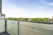 Balcony with frosted glass railing and view of tree tops.
