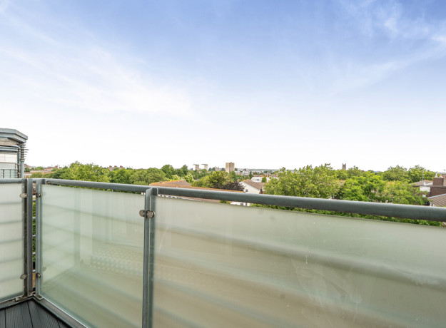 Balcony with frosted glass railing and view of tree tops.