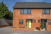 Exterior view of two-storey red brick house with yellow front door and boundary with low brick wall