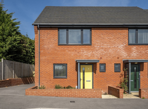 Exterior view of two-storey red brick house with yellow front door and boundary with low brick wall