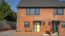 Exterior view of two-storey red brick house with yellow front door and boundary with low brick wall