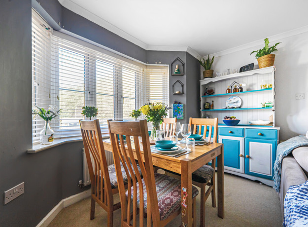 Dining space with wooden table and chairs positioned by bay windows and shelving