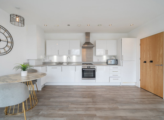 Kitchen and dining area with white cabinets, appliances, wood-effect flooring, and dining table