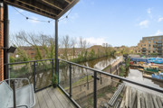 Balcony with metal railing and wooden decking, overlooking nearby homes and greenery