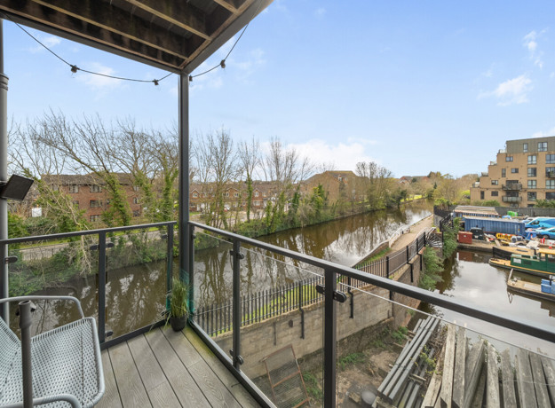 Balcony with metal railing and wooden decking, overlooking nearby homes and greenery