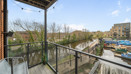 Balcony with metal railing and wooden decking, overlooking nearby homes and greenery